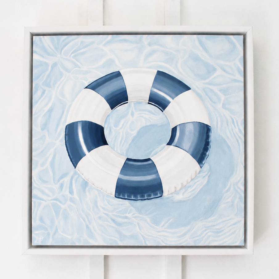 Original oil painting of a blue and white pool float floating on shimmering water, framed in a white wood float frame by coastal artist Laurie Duncan.